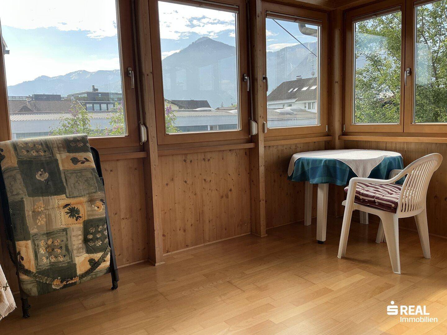 Heller Wintergarten mit Holzverkleidung, großen Fenstern und Bergblick.