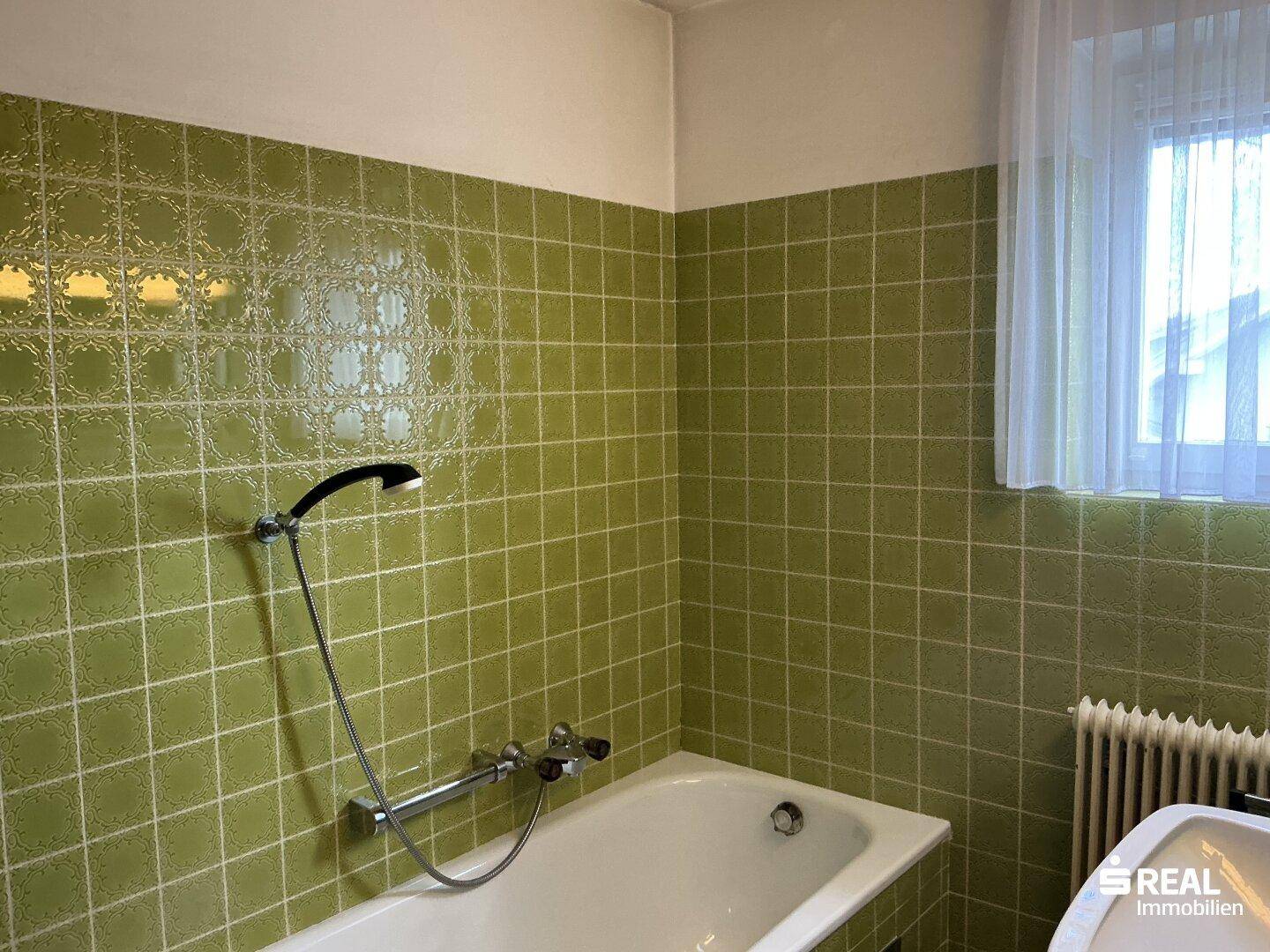 Badezimmer mit grünen Fliesen, Badewanne und Fenster für natürliche Belüftung.