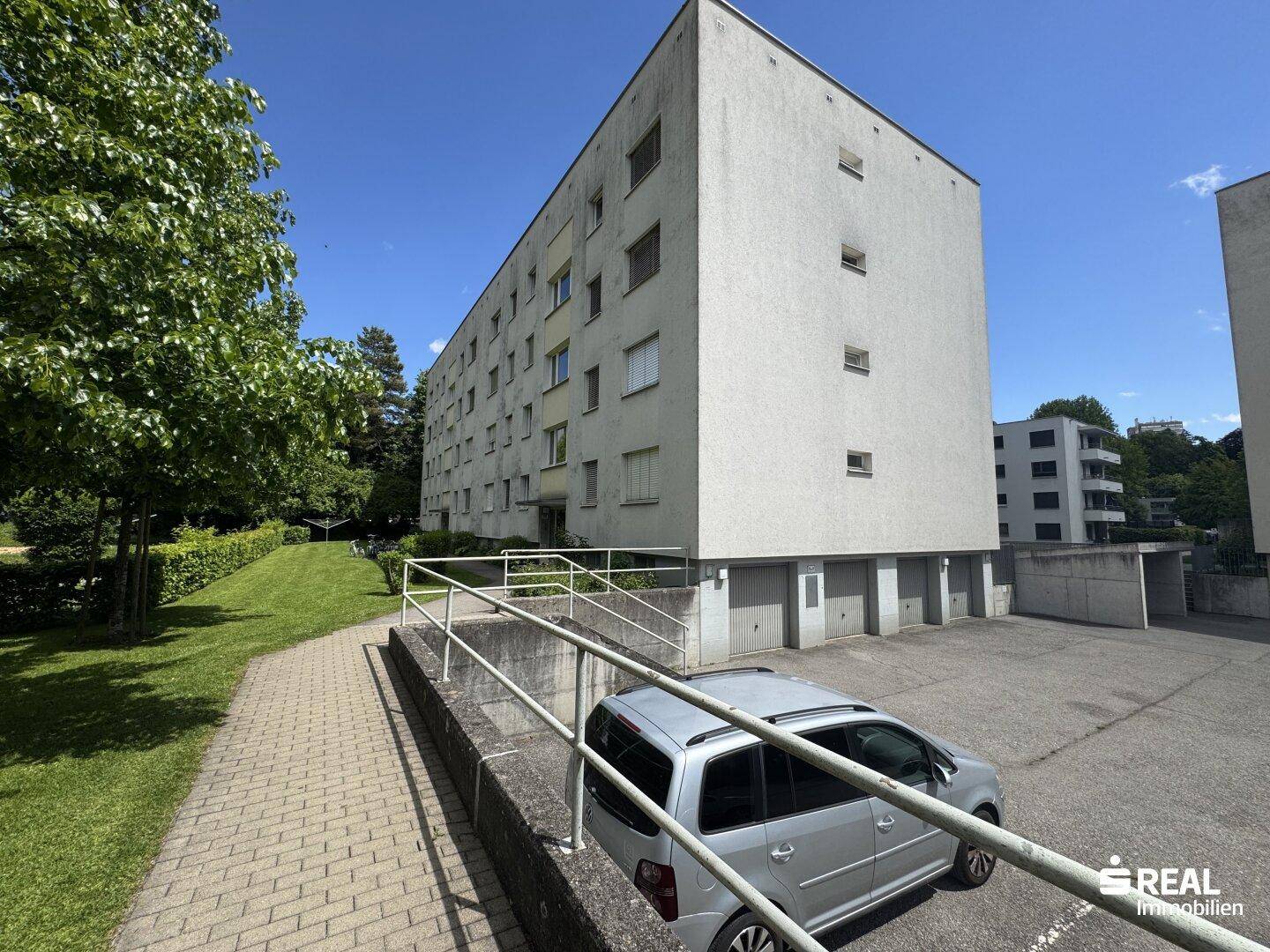 Mehrstöckiges Wohngebäude mit Garagen im Erdgeschoss und Außenparkplätzen.