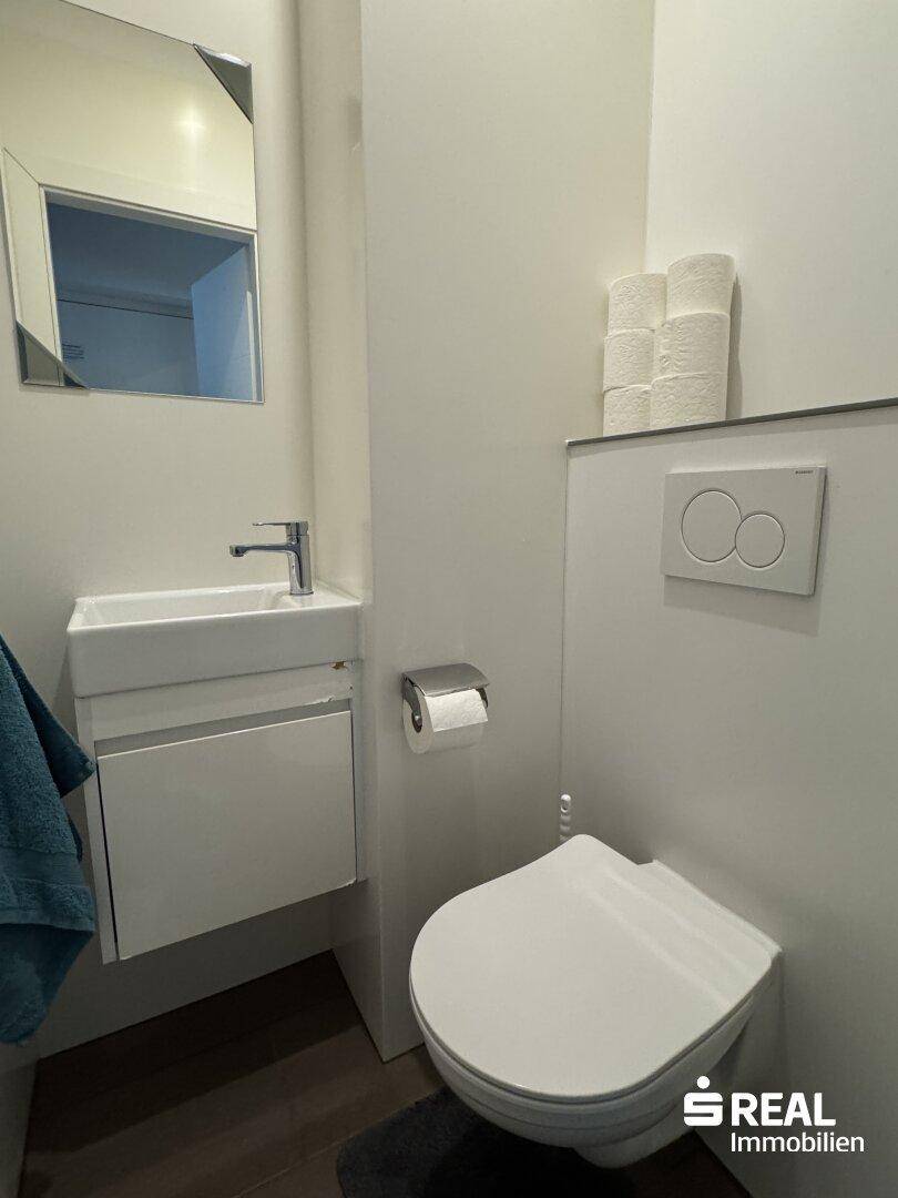 Kompaktes Gäste-WC mit wandhängender Toilette und kleinem Handwaschbecken.