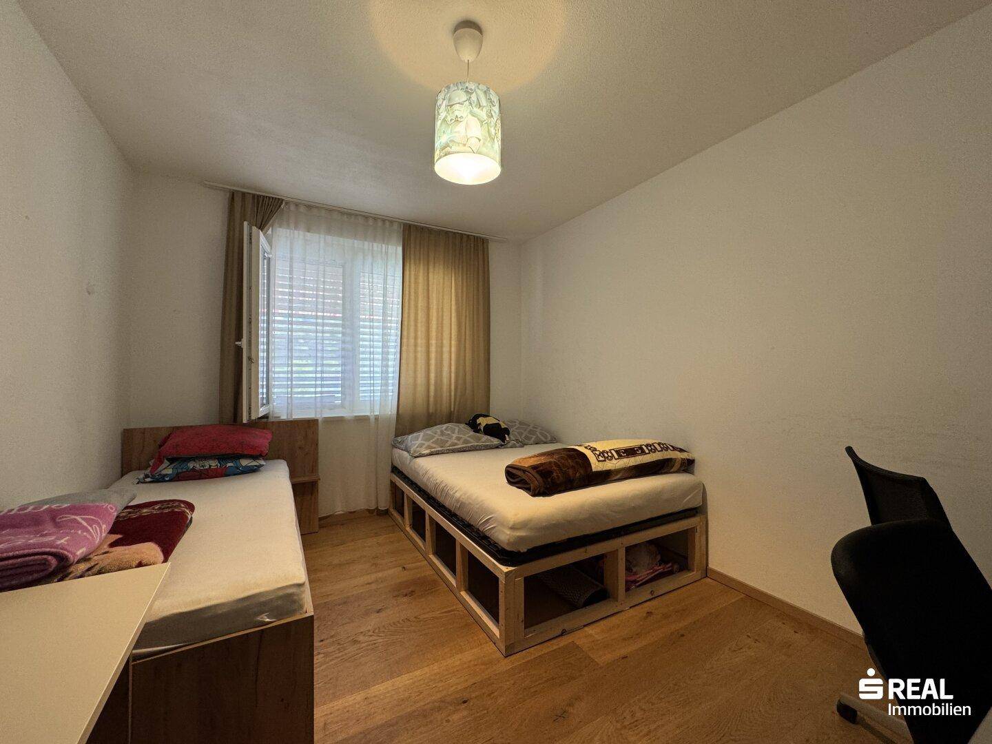 Helles Schlafzimmer mit zwei Einzelbetten, Holzfußboden und Fenster mit Jalousien.