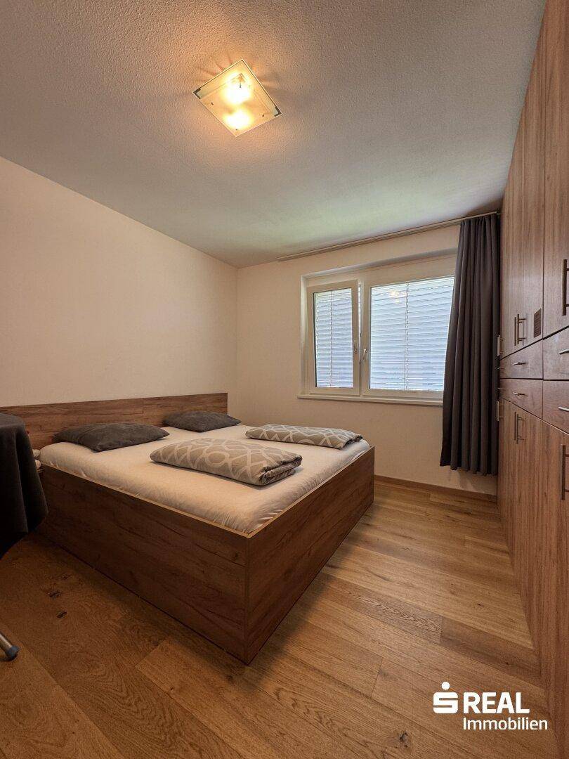 Gemütliches Schlafzimmer mit Doppelbett, Holzschrank und Fenster mit Vorhängen.