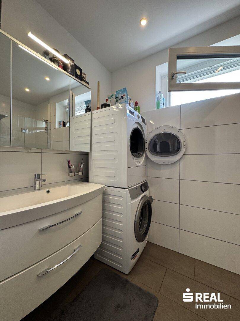 Modernes Badezimmer mit Waschbecken, Spiegelschrank und gestapelter Waschmaschine/Trockner.