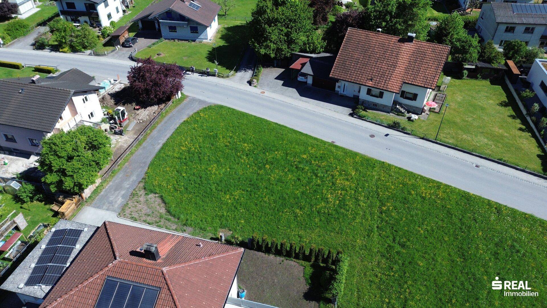 Übersicht aus der Vogelperspektive des grünen Baugrundstücks, umgeben von Wohnbebauung und Straßen.