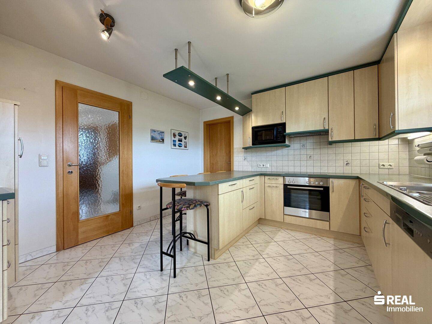 Funktionale Küche mit hellen Holzfronten, Fliesenboden und einem praktischen Tresen mit Sitzgelegenheiten.