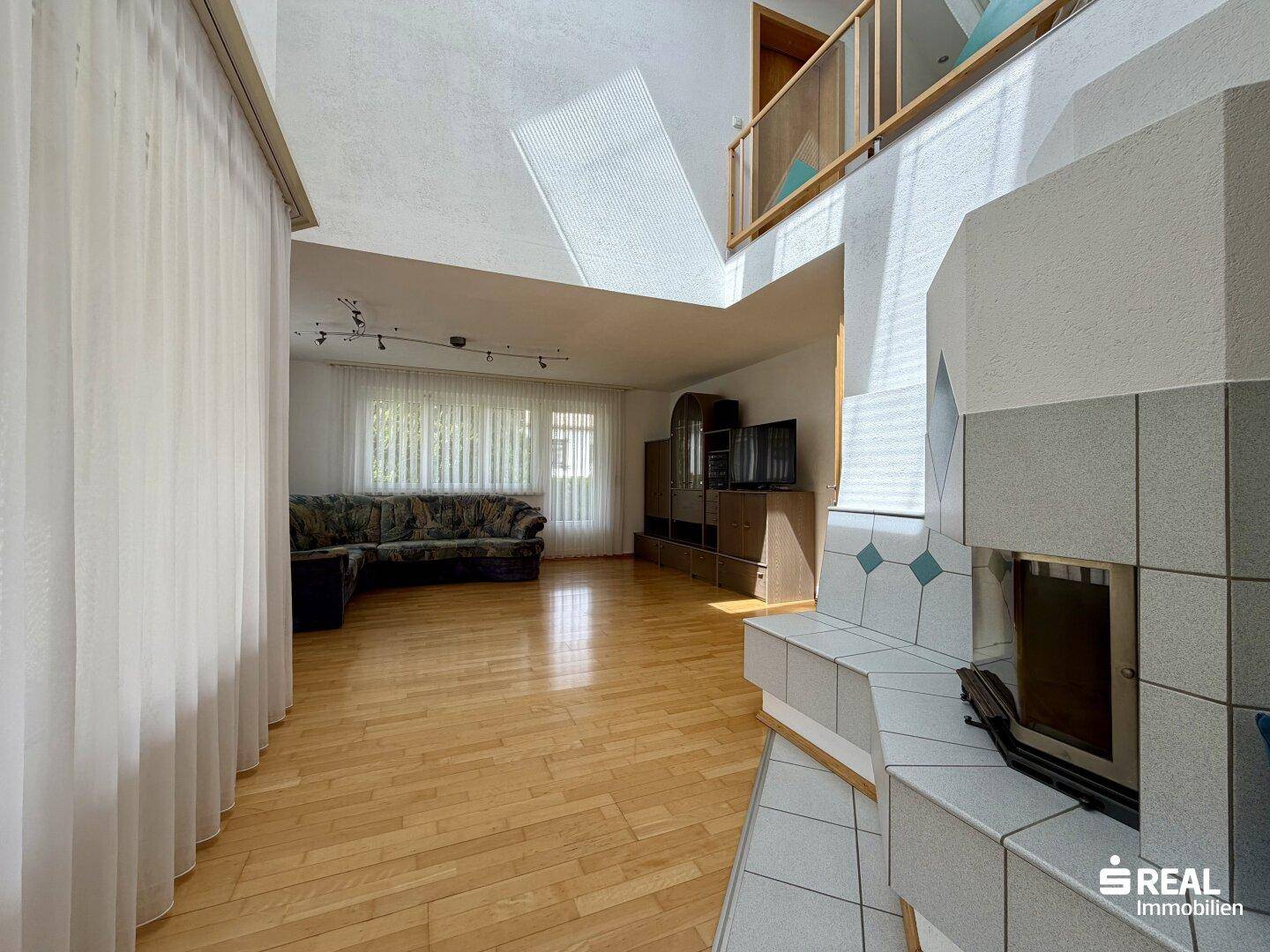 Gemütliches Wohnzimmer mit Parkettboden, großem Fenster und einem gefliesten Kaminofen.