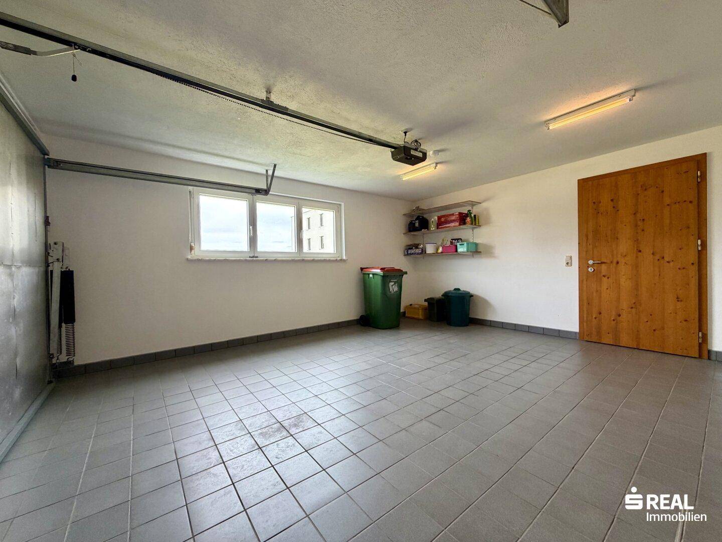 Geräumige Garage mit Fliesenboden, Fenster und automatischem Torantrieb für Fahrzeuge oder Lagerung.