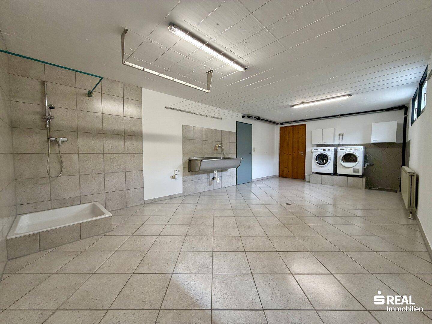 Großer Hauswirtschaftsraum mit Fliesenboden, Dusche, Waschbecken und Anschlüssen für Waschmaschinen und Trockner.