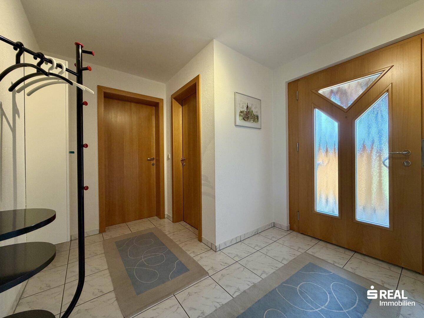 Eingangsbereich mit Fliesenboden, Garderobe und Holztüren, die zu weiteren Räumen führen.