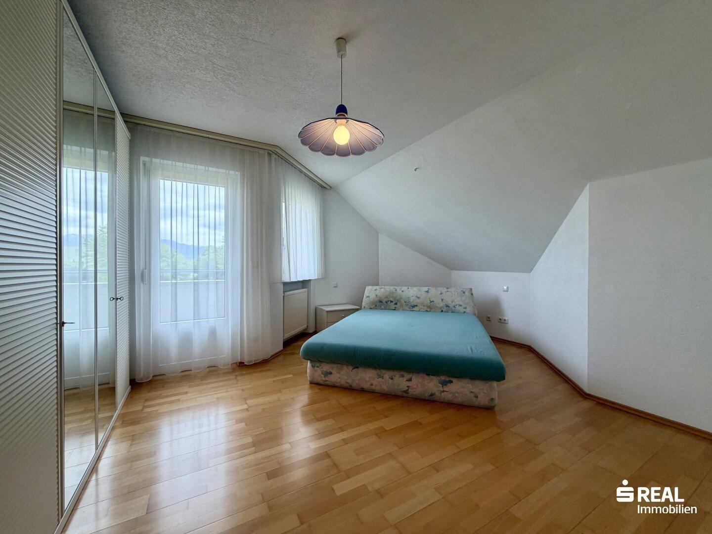 Schlafzimmer im Dachgeschoss mit Parkettboden, großem Fenster und einem Kleiderschrank mit Spiegelfronten.