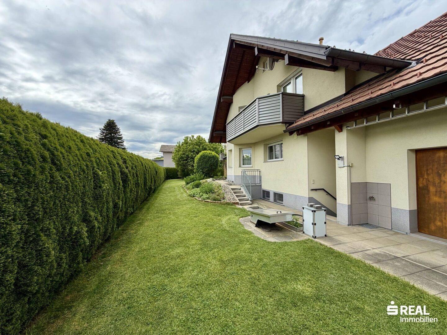 Seitlicher Gartenbereich mit Hecke, Zugang zum Haus und einem kleinen Balkon im Obergeschoss.