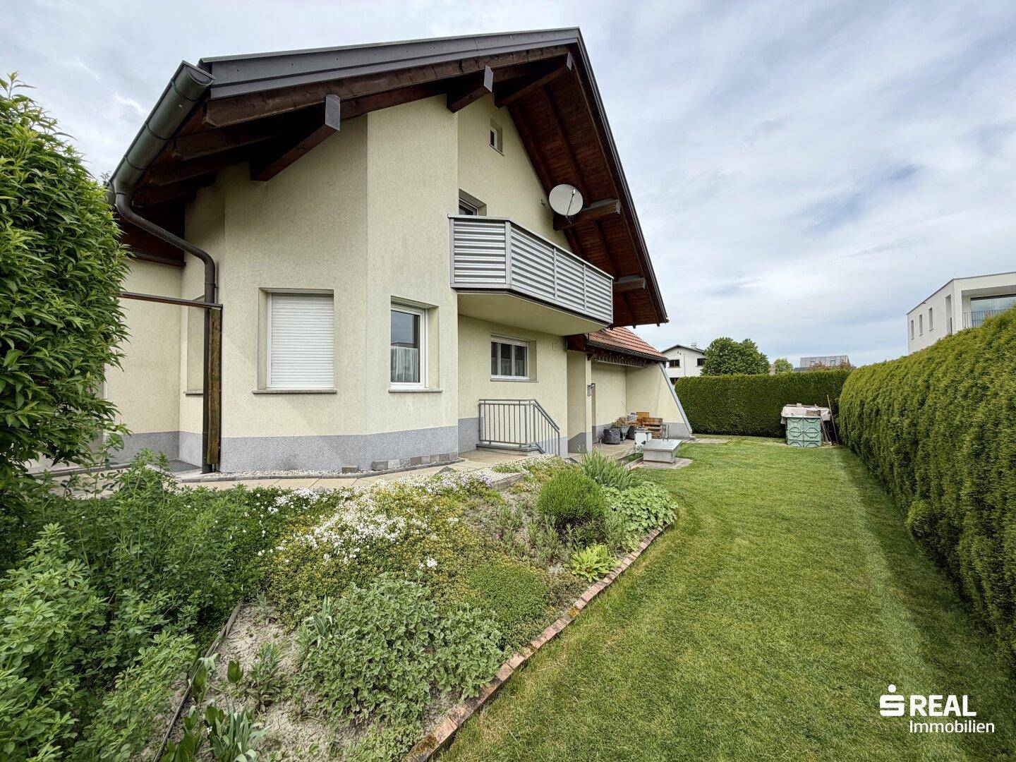 Seitenansicht des Hauses mit gepflegtem Gartenbereich, Rasenfläche und blühenden Blumenbeeten.