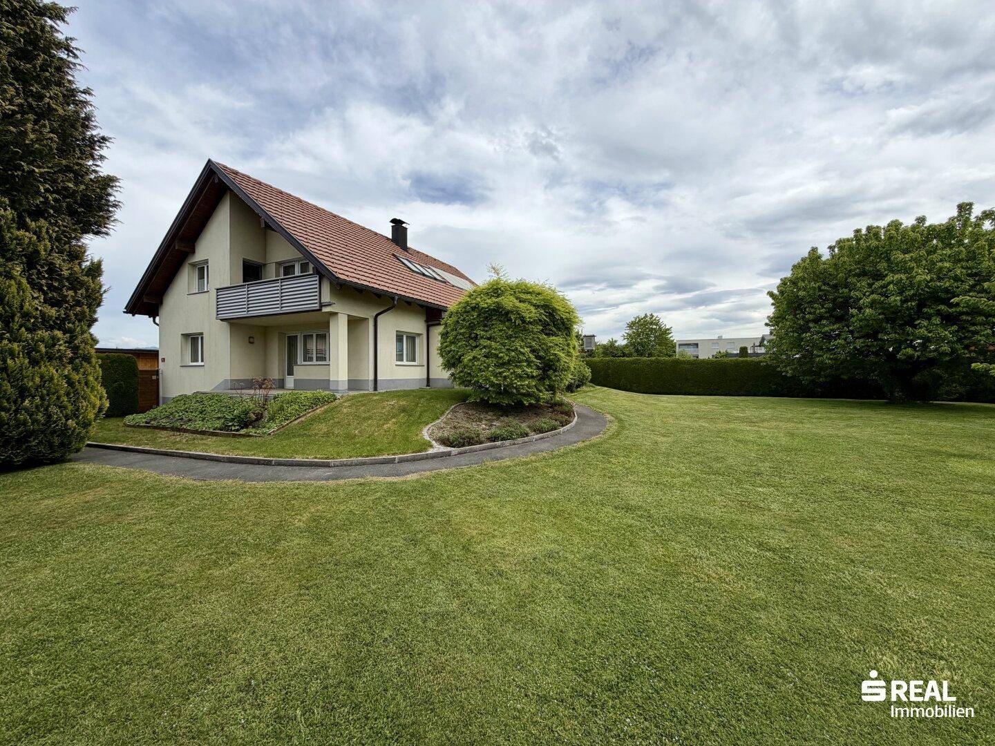 Seitenansicht des Einfamilienhauses mit Balkon und weitläufigem, gepflegtem Rasenbereich.