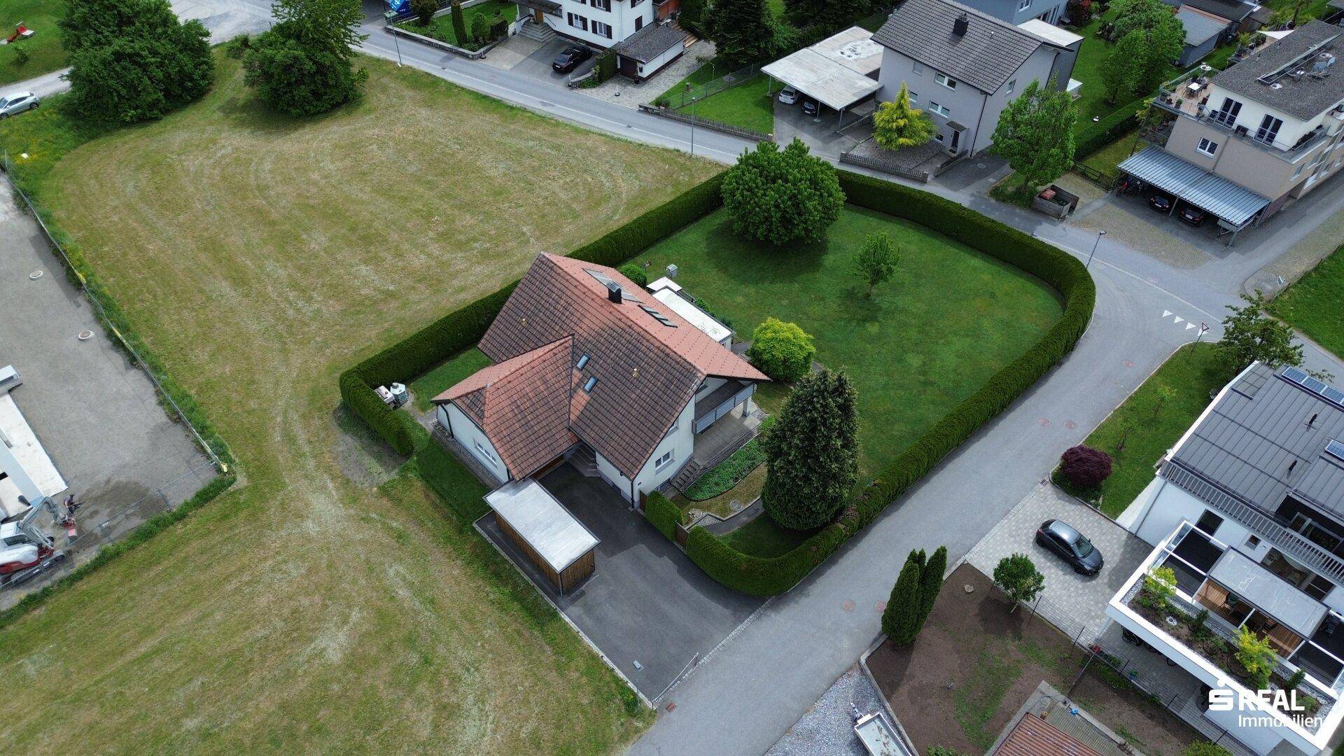 Luftaufnahme des Hauses mit gepflegtem Garten, umgeben von einer dichten Hecke und Rasenflächen.