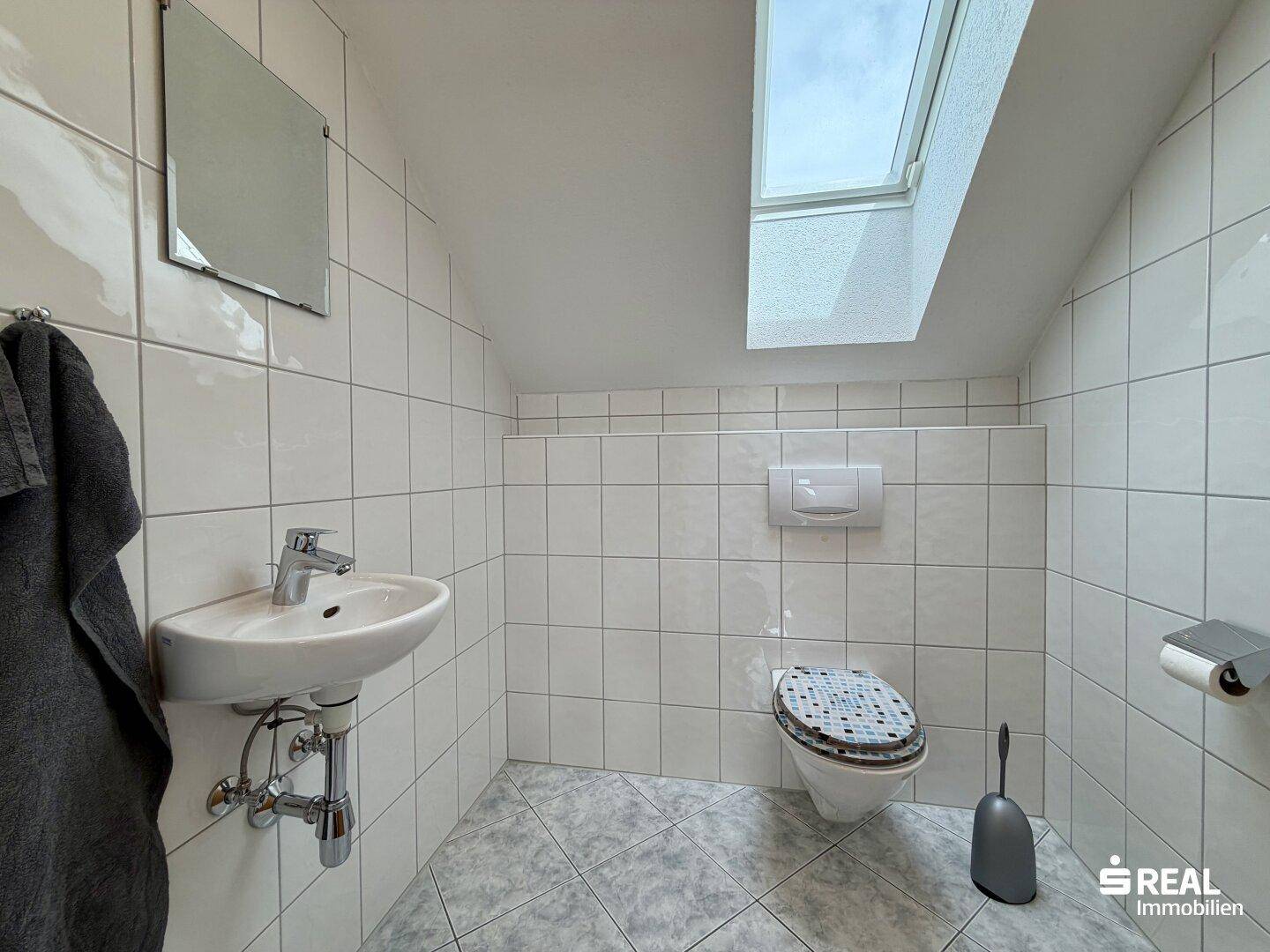 Kleines WC im Dachgeschoss mit Dachfenster, wandhängendem WC und Waschbecken.