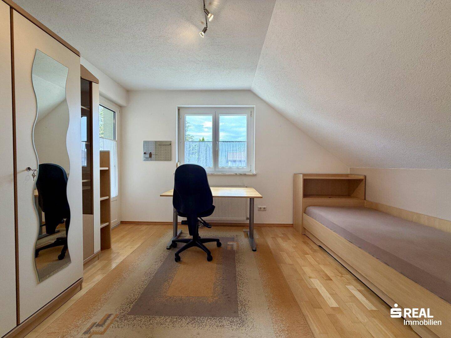 Helles Zimmer im Dachgeschoss mit Parkettboden, Schreibtisch und einem Einzelbett.