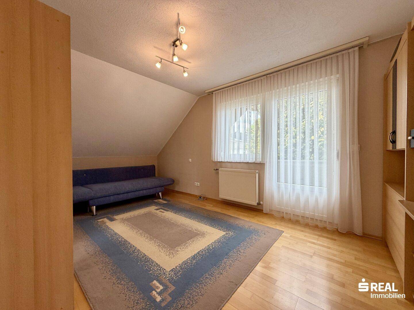 Geräumiges Schlafzimmer im Dachgeschoss mit Parkettboden, Sofa und einem großen Fenster.