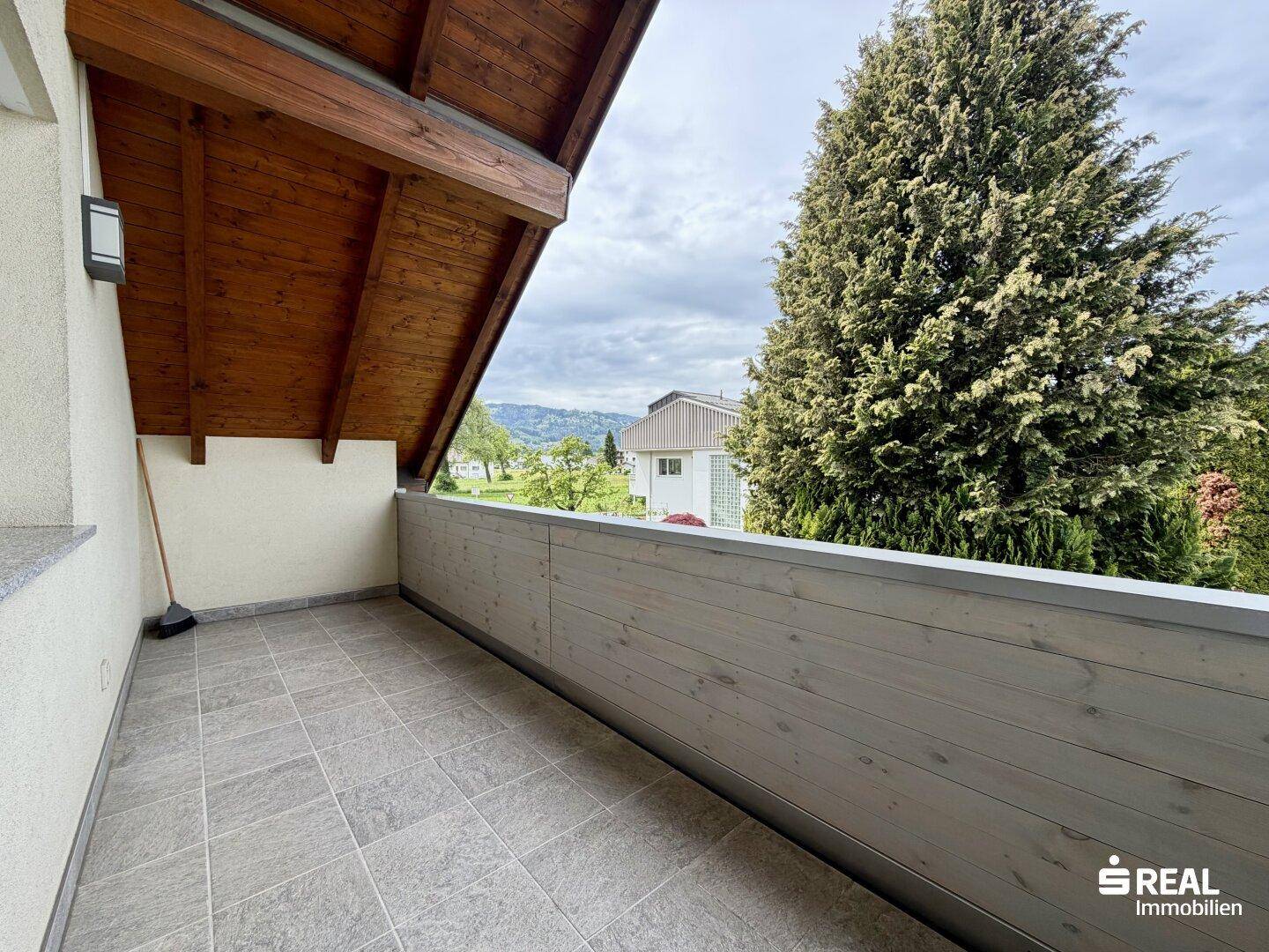 Überdachter Balkon mit Fliesenboden und Holzverkleidung, bietet einen Blick ins Grüne.