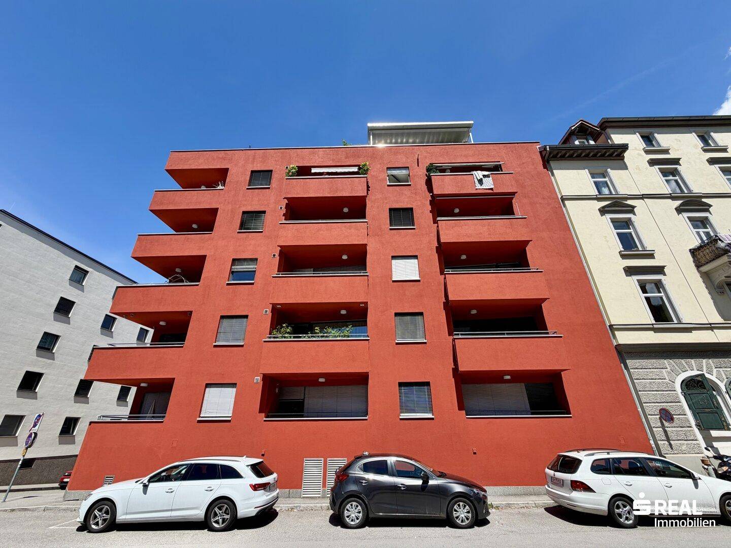 Modernes Wohngebäude mit auffälliger roter Fassade, Balkonen und vielen Fenstern.