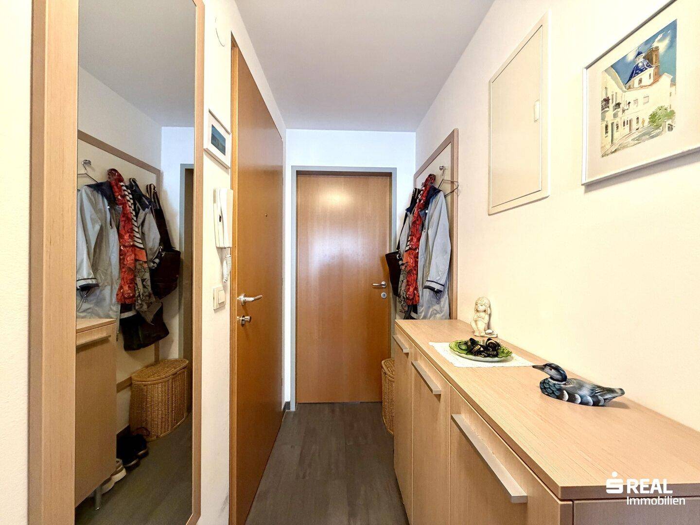 Heller Eingangsbereich mit Garderobe, Spiegel und praktischen Holzmöbeln für Stauraum.