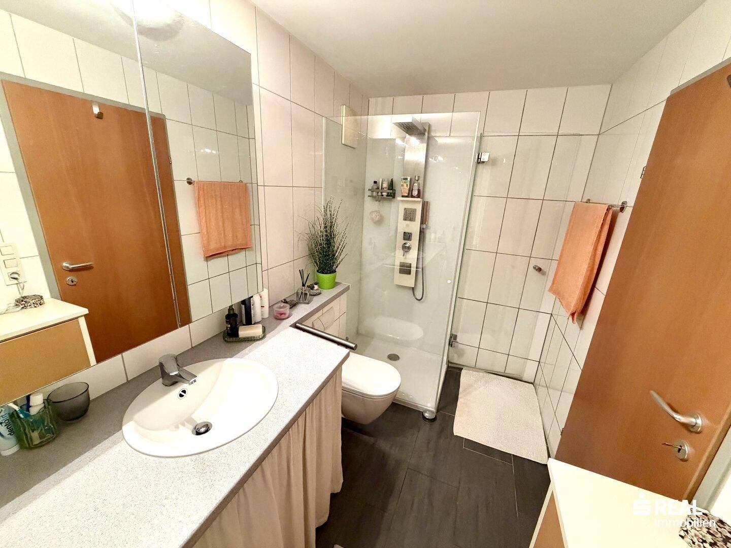 Modernes Badezimmer mit Duschkabine, Waschbecken und WC, gefliest in Weiß und Dunkelgrau, gepflegt.