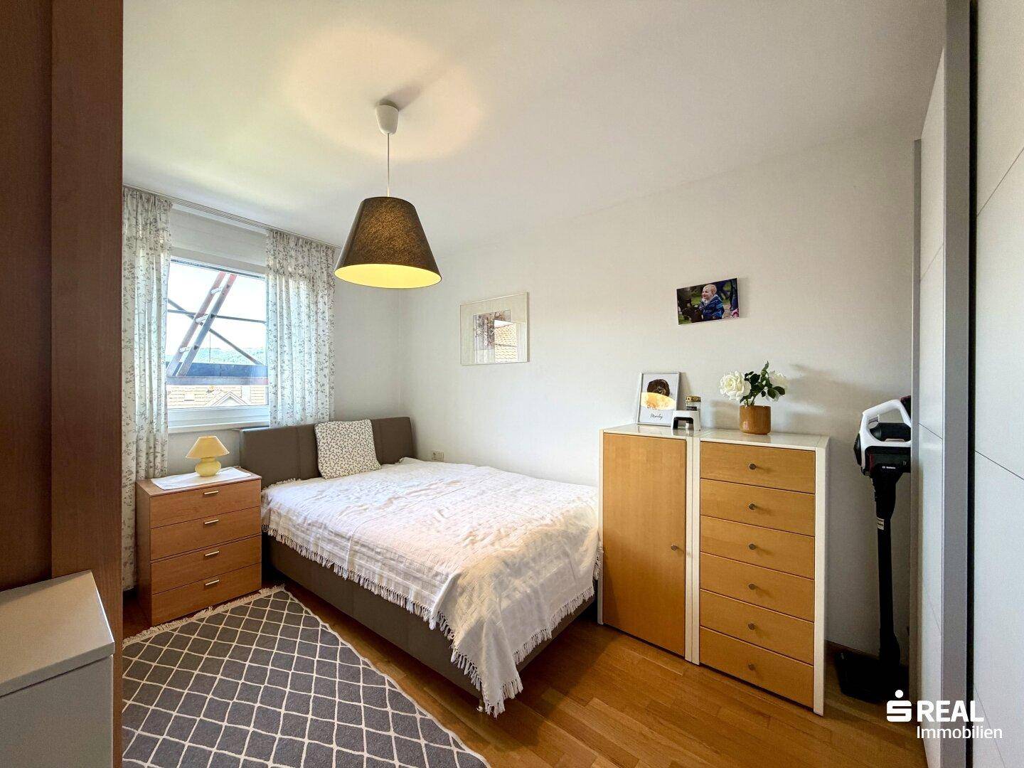 Schlafzimmer mit Holzboden, Doppelbett und Kommoden, hell durch Fenster, gemütlich und einladend.
