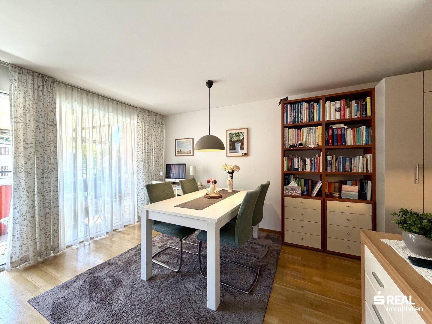 Geräumiger Wohn-Essbereich mit Holzboden, großem Fenster und direktem Zugang zum Balkon.