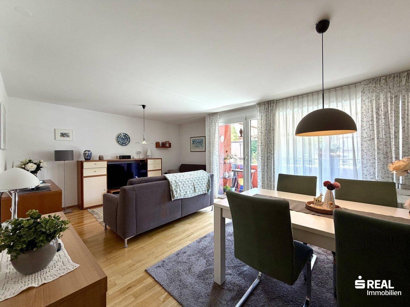 Gemütlicher Wohn-Essbereich mit Holzboden, Sofa und Esstisch, hell durch große Fenster und Balkonzugang.