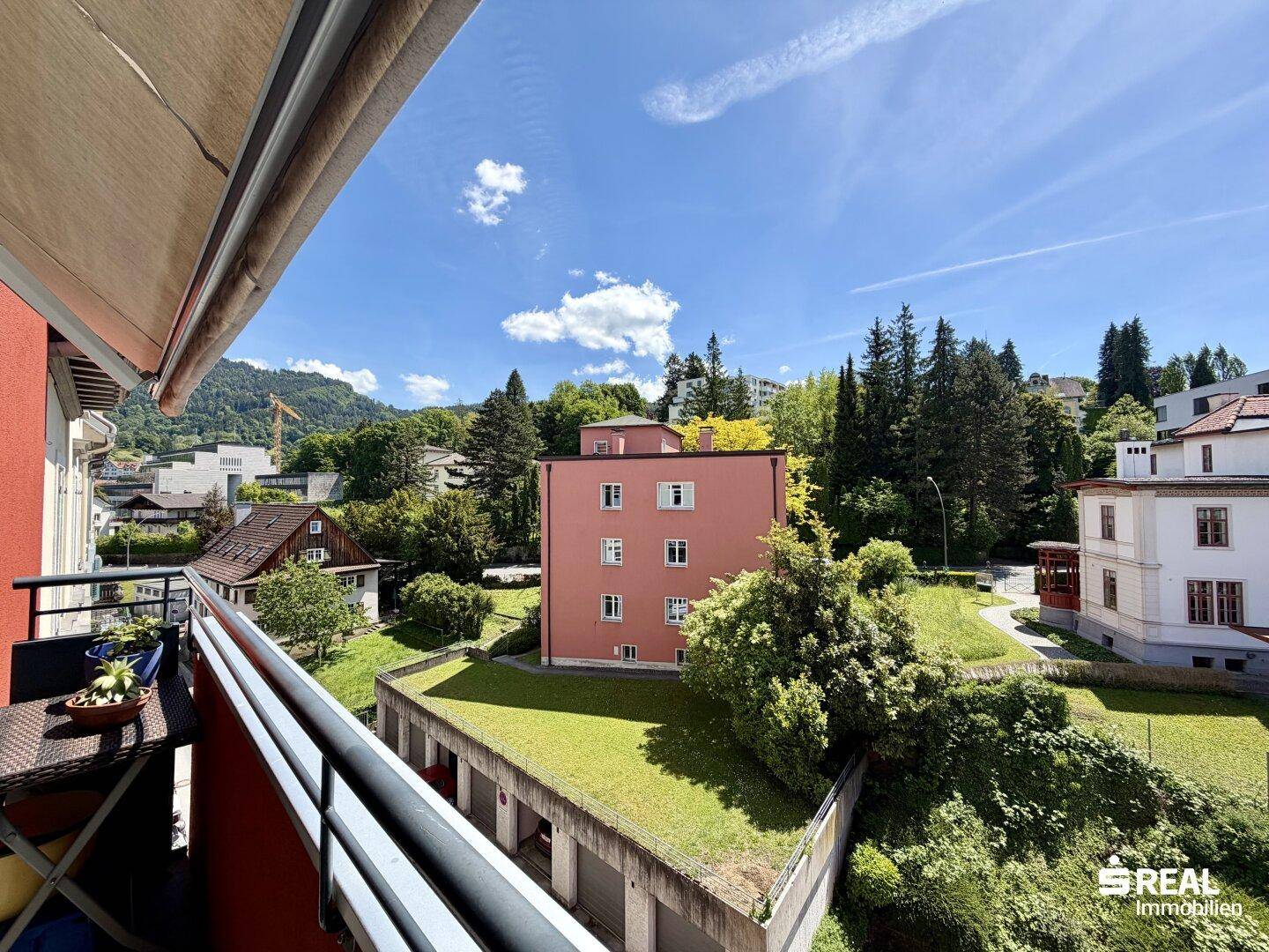 Sonniger Balkon mit Markise und weitem Blick ins Grüne und auf umliegende Gebäude, ideal zum Entspannen.