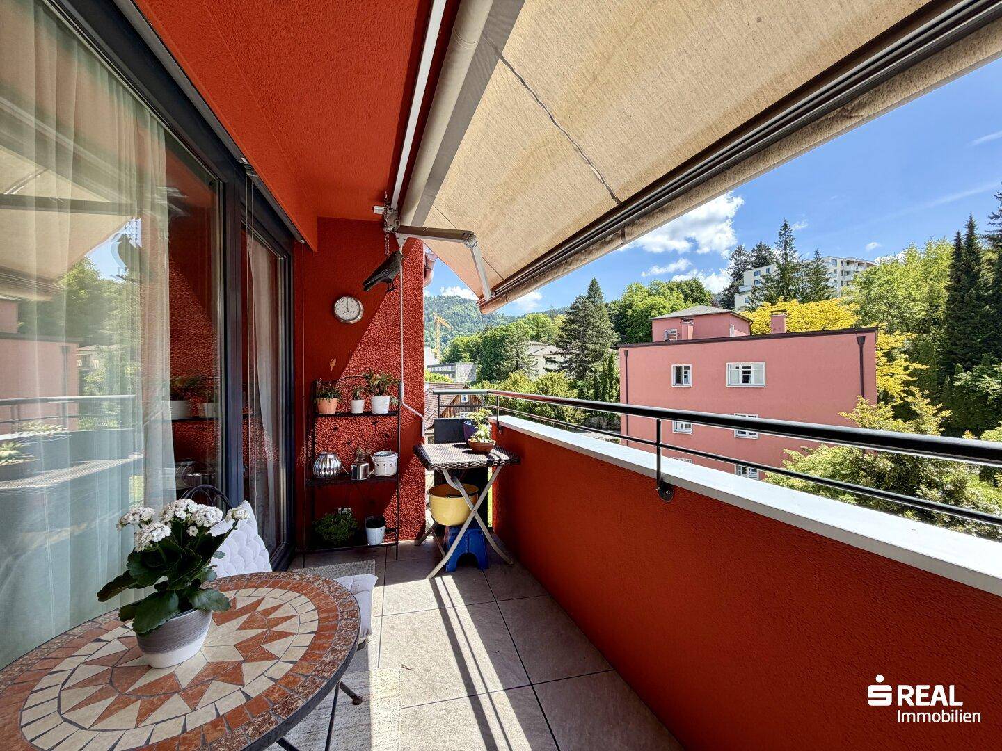 Sonniger Balkon mit Markise, kleinem Tisch und Blick ins Grüne, ideal zum Entspannen im Freien.