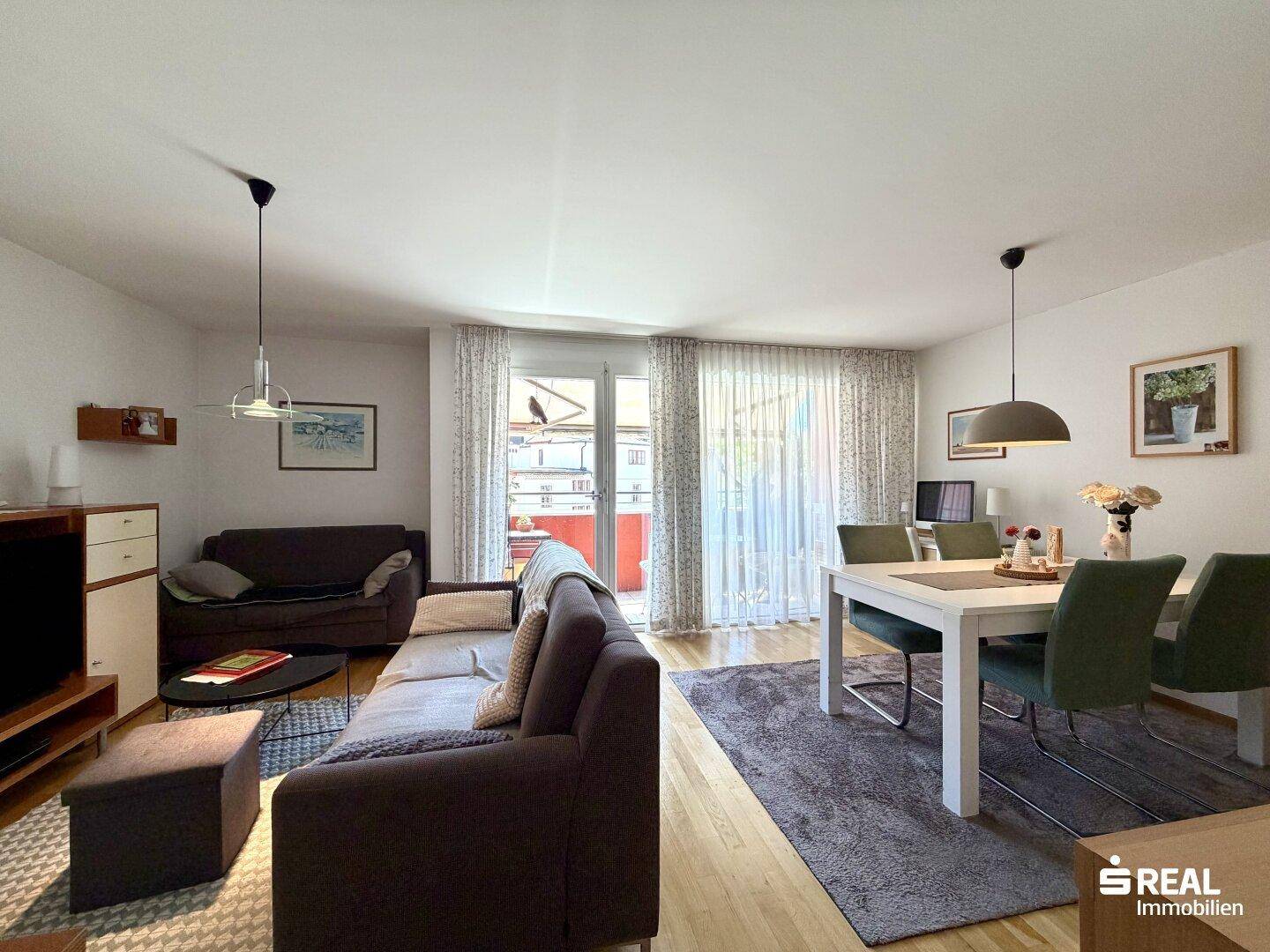 Heller Wohn- und Essbereich mit bequemen Sofas, Esstisch und direktem Balkonzugang.