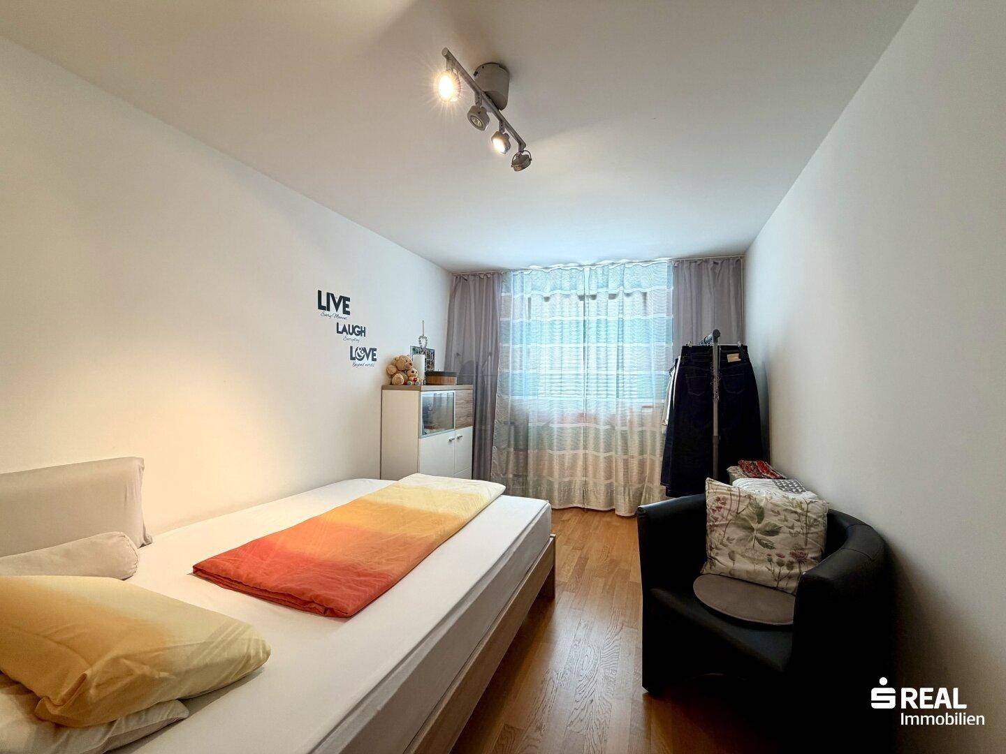 Helles Schlafzimmer mit Einzelbett und Fenster, schlicht und funktional eingerichtet, mit Holzboden.