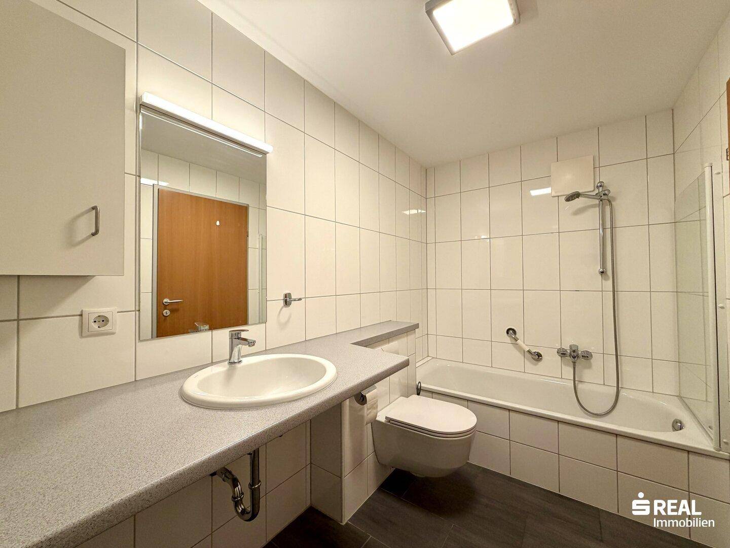 Badezimmer mit Badewanne, Waschbecken und WC, gefliest in Weiß und Dunkelgrau, funktional und sauber.