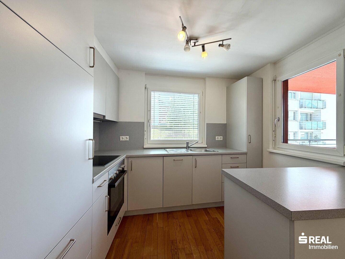 Helle Küche mit Fenster, grauen Schränken, Holzboden und moderner Ausstattung.