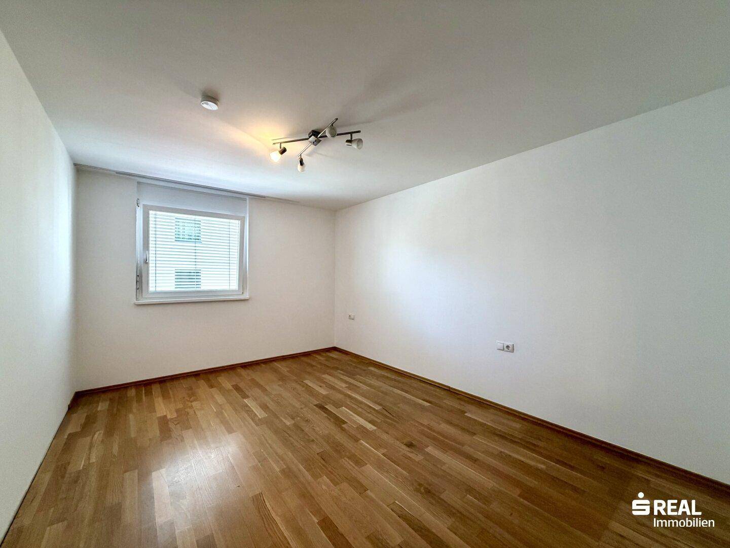 Helles Schlafzimmer mit Holzboden, großem Fenster und neutralen Wänden, ideal für individuelle Gestaltung.