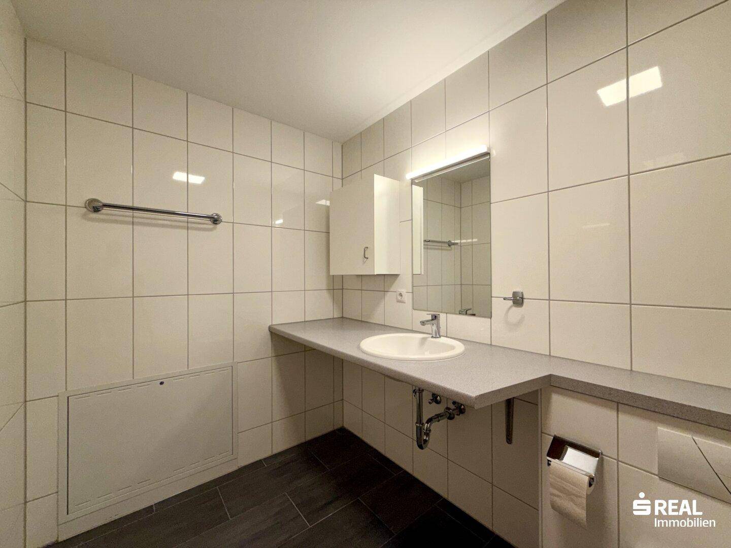 Kleines Badezimmer mit Waschbecken und WC, komplett gefliest in Weiß, funktional und sauber.