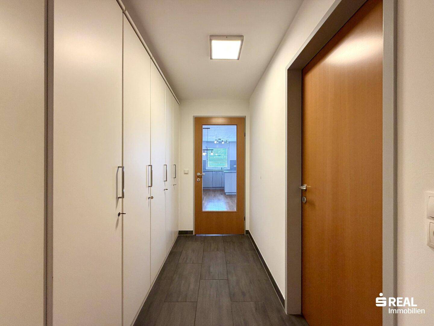 Langer Flur mit Einbauschränken und Blick in die Küche durch eine Glastür.