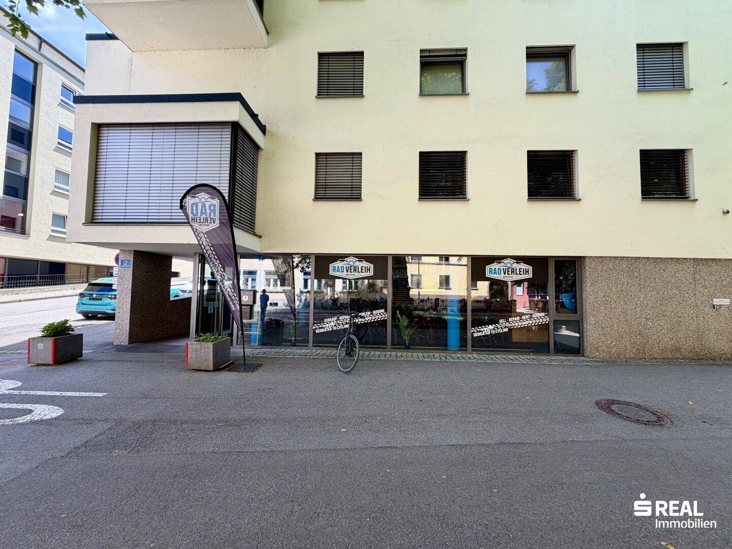Geschäftsfassade im Erdgeschoss eines modernen Gebäudes mit Schaufenstern und Werbetafeln.
