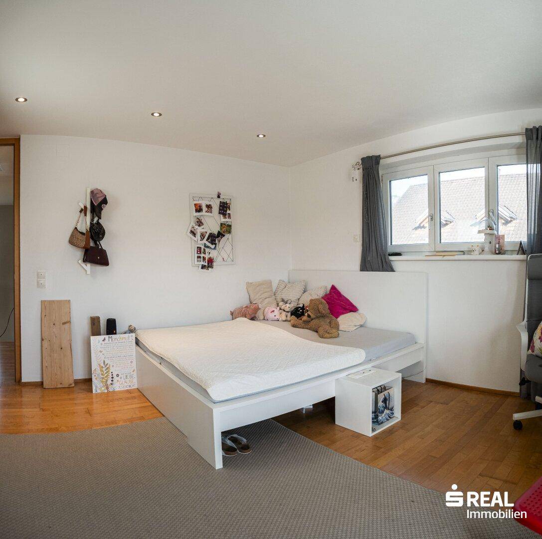 Helles Schlafzimmer mit Holzboden, großem Bett und Fenster mit Blick nach draußen.