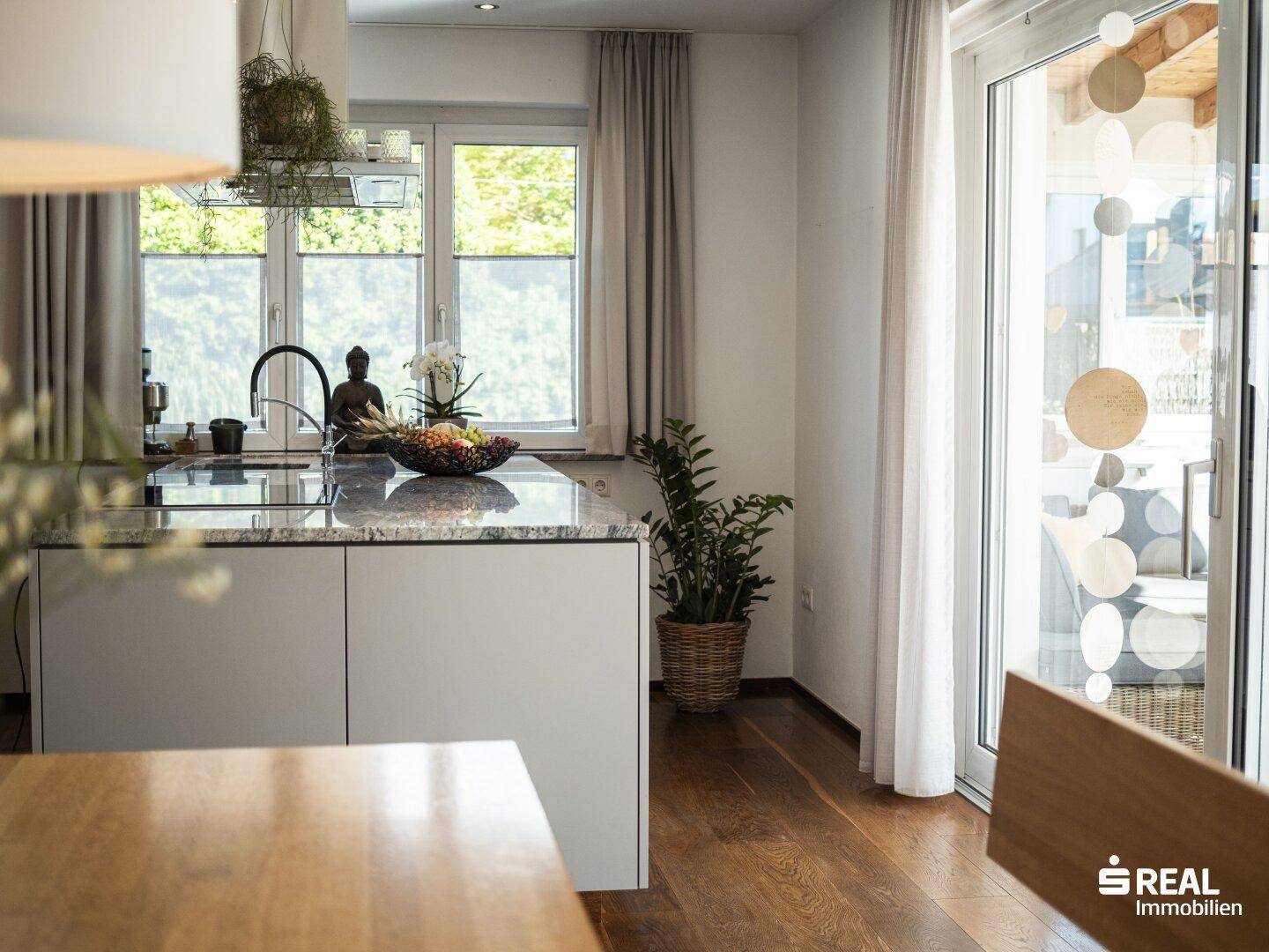 Moderne Küche mit Kücheninsel und Blick durch die Terrassentür in den Garten.