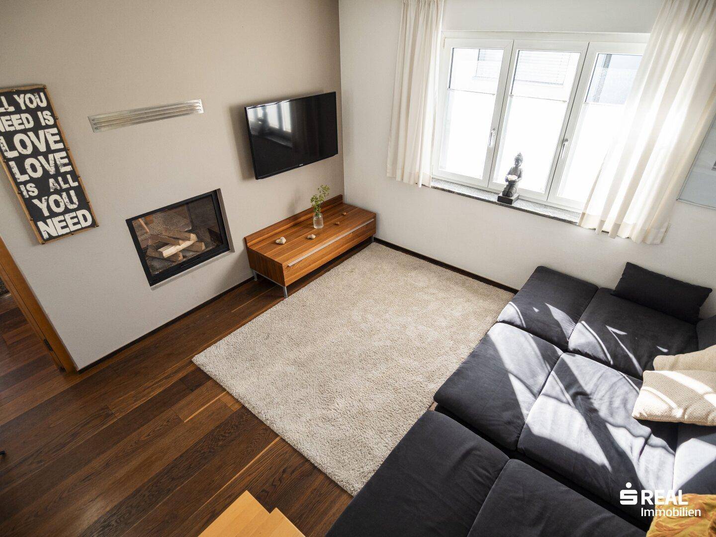 Helles Wohnzimmer mit Holzboden, Kamin und modernem Sofa, ideal zum Entspannen.