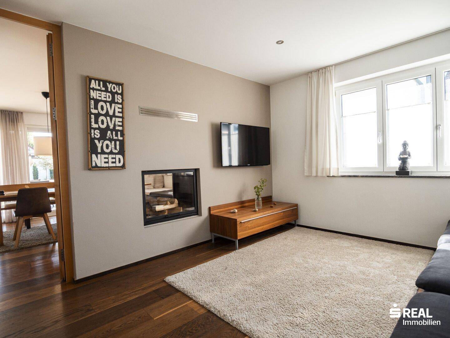 Gemütliches Wohnzimmer mit Kamin, Holzboden und Blick in den Essbereich.