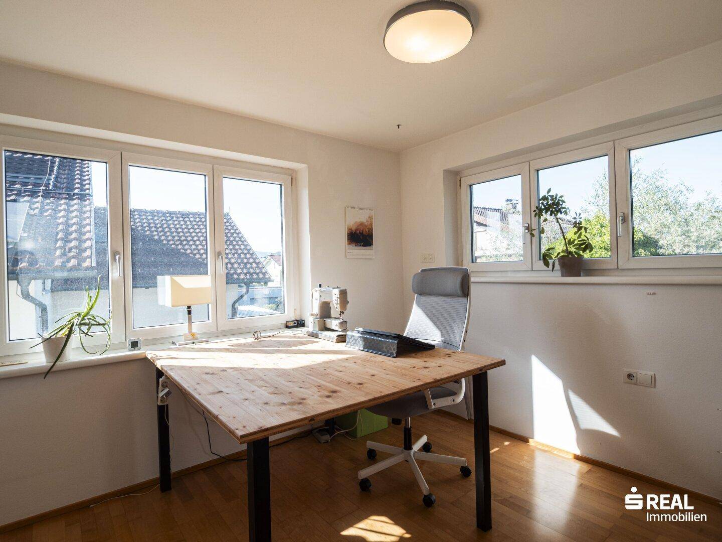 Helles Arbeitszimmer mit großem Schreibtisch und Blick ins Grüne durch mehrere Fenster.