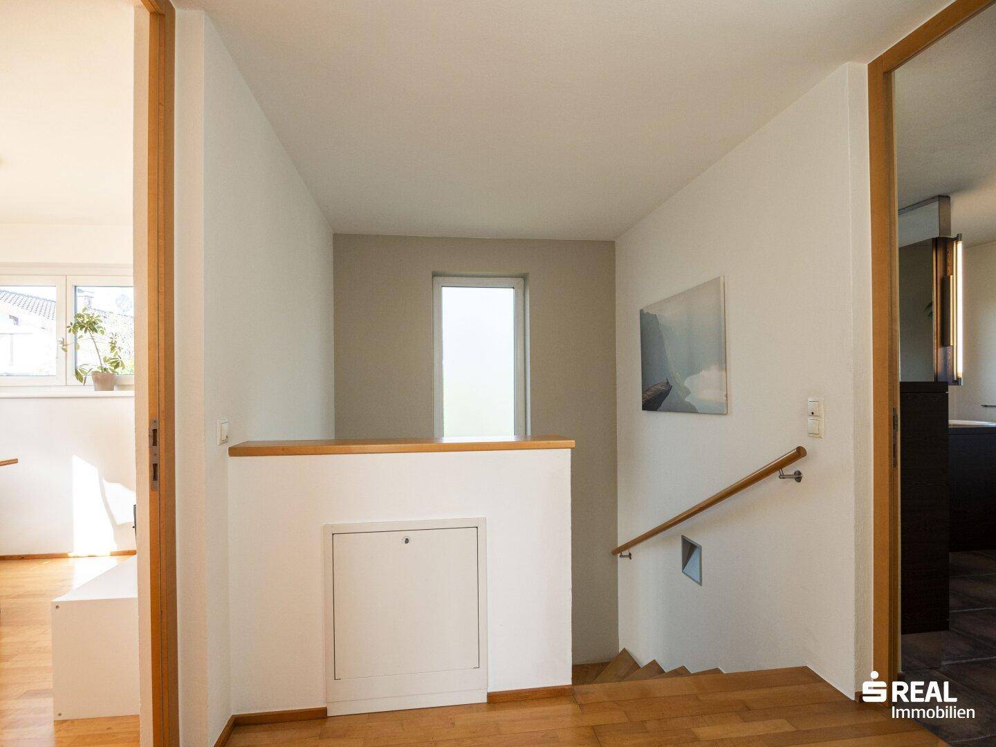 Heller Flur mit Holztreppe und kleinem Fenster, der die verschiedenen Ebenen verbindet.