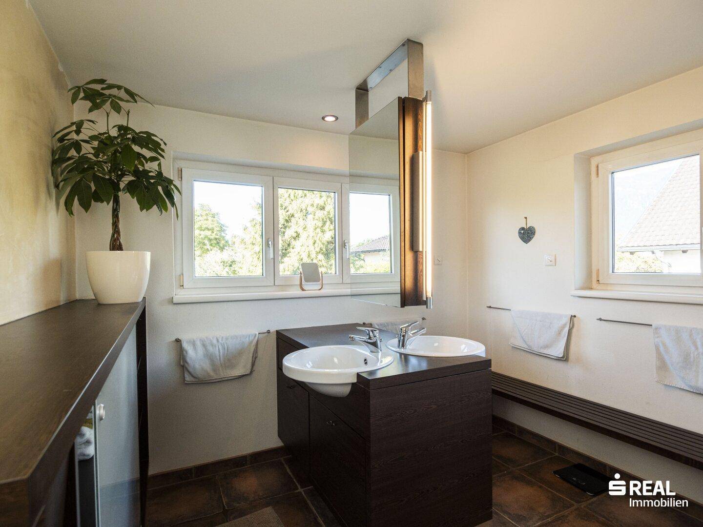 Geräumiges Badezimmer mit Doppelwaschbecken, Badewanne und Fenster mit Grünblick.