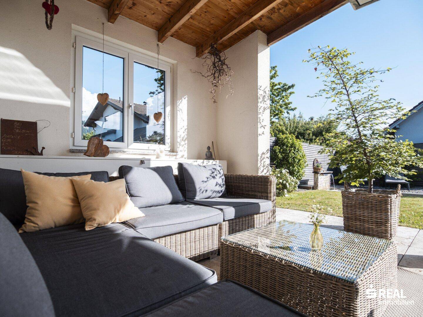 Überdachte Terrasse mit gemütlichen Rattanmöbeln und Blick in den Garten.
