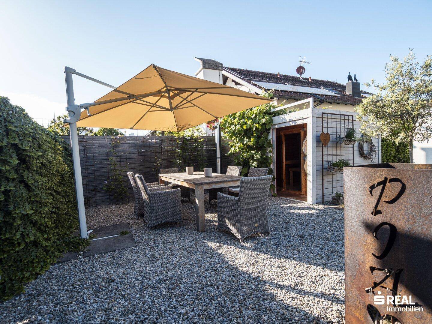 Weitläufiger Gartenbereich mit Essplatz, Sonnenschirm und kleiner Sauna.