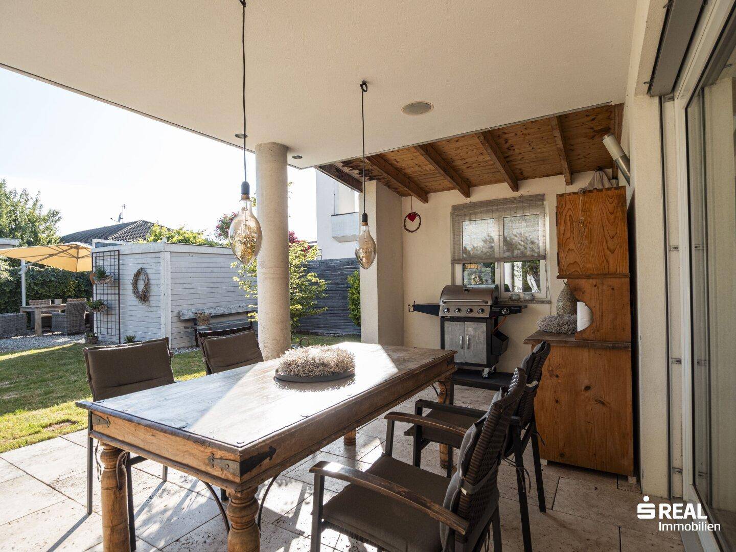Überdachte Terrasse mit Essbereich und Grill, angrenzend an den Garten.