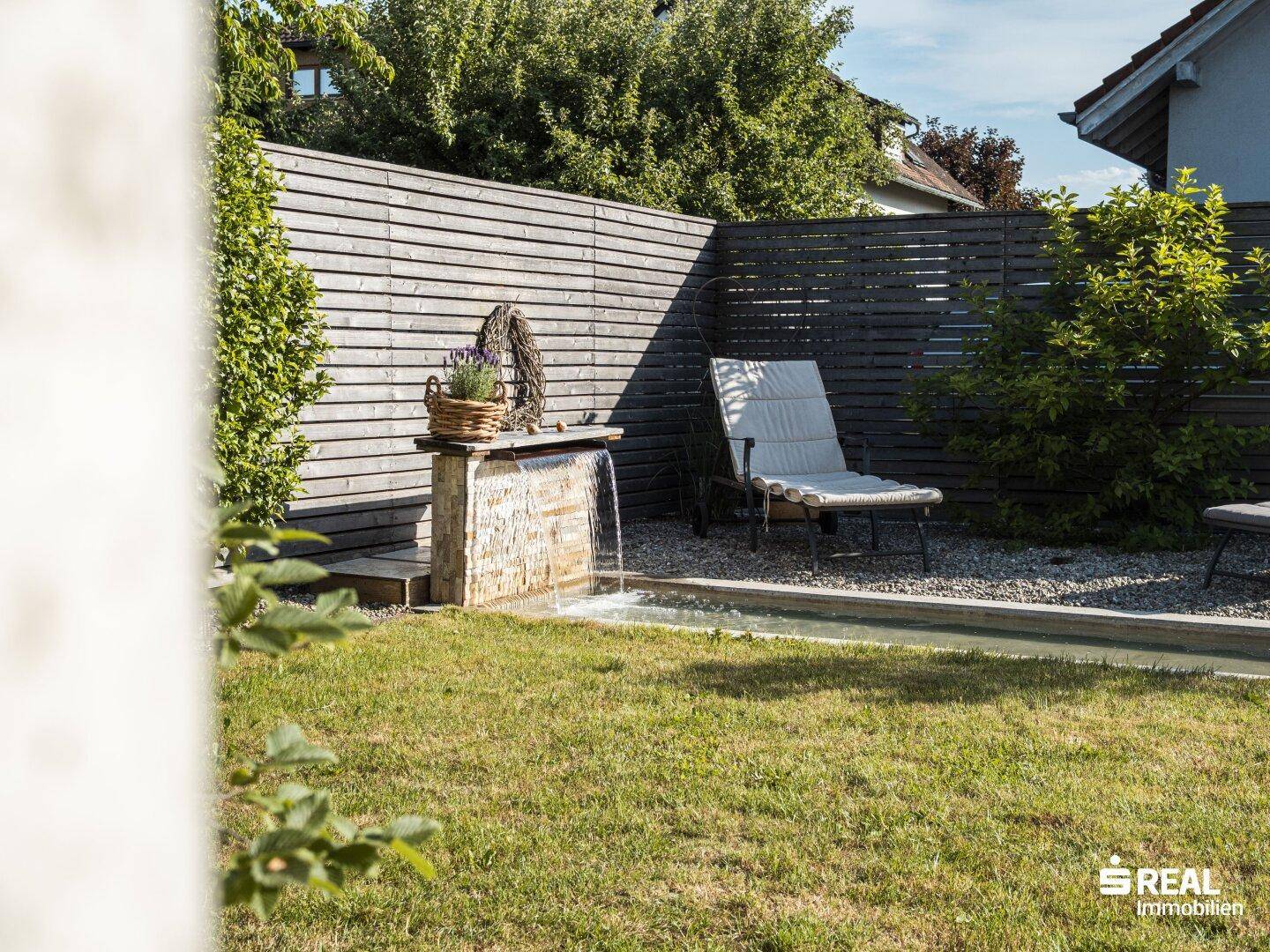 Gepflegter Garten mit Rasenfläche, Wasserbecken und Liegestuhl für Entspannung.