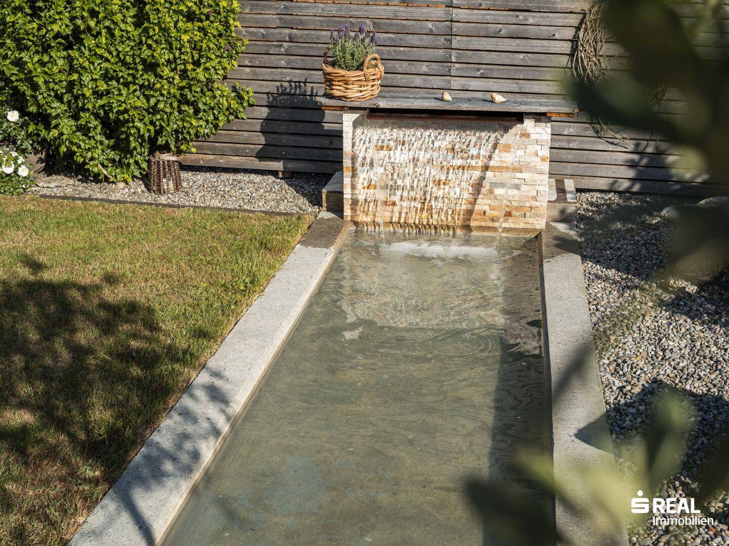 Detailansicht des Wasserbeckens im Garten mit Steinmauer und Pflanzen.